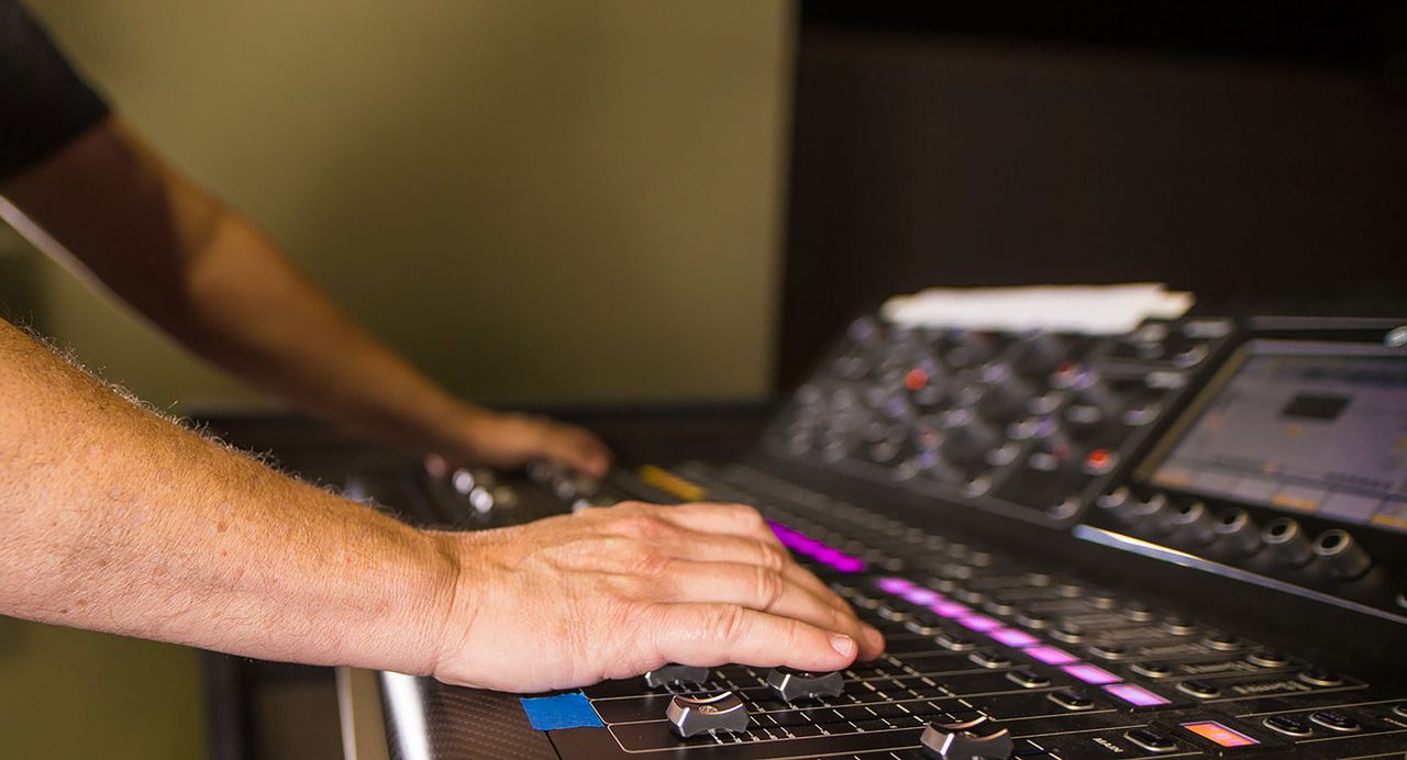 Hands of a sound engineer adjusting levels on an audio mixer in a professional recording studio.